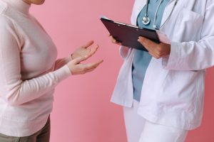 Doctor talking to patient standing against pink background.